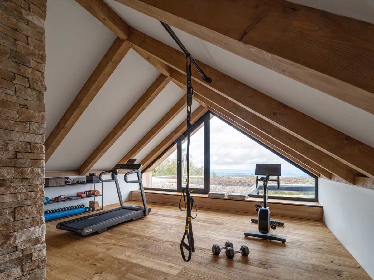 Domácí posilovna v podkroví s dřevěnou podlahou a výhledem na okolní krajinu.