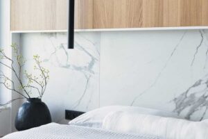 Detail ložnice s dřevěným obložením, mramorovým panelem a černým závěsným svítidlem