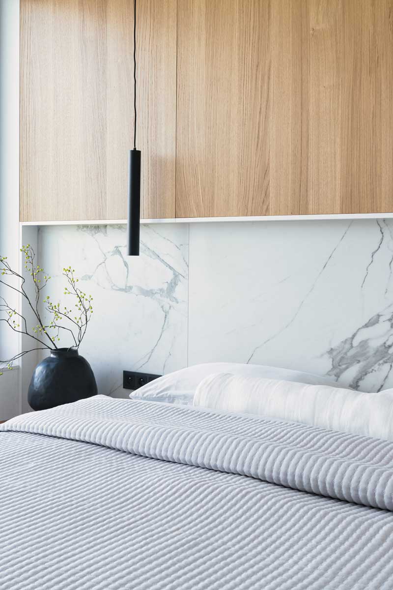 Detail ložnice s dřevěným obložením, mramorovým panelem a černým závěsným svítidlem