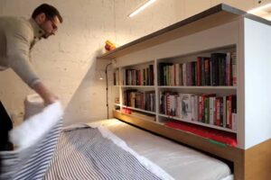 Výsuvná postel uložená pod vyvýšenou kuchyňskou platformou v garsonce.