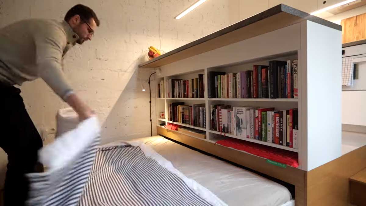 Výsuvná postel uložená pod vyvýšenou kuchyňskou platformou v garsonce.