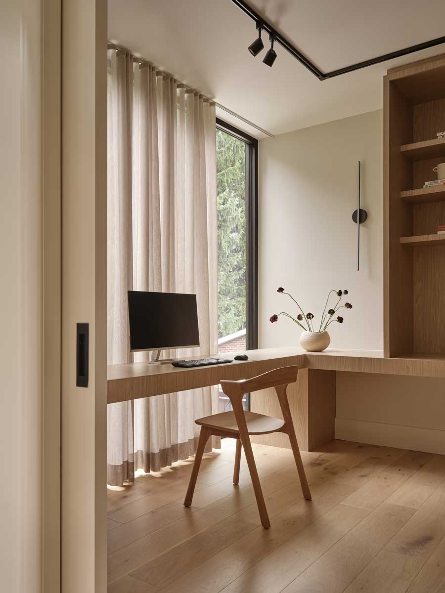 Pracovní kout s dřevěným stolem u okna, otevřenými policemi a minimalistickým osvětlením