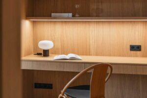 Detail vestavěného psacího stolu z dubového dřeva s policemi a integrovaným osvětlením.