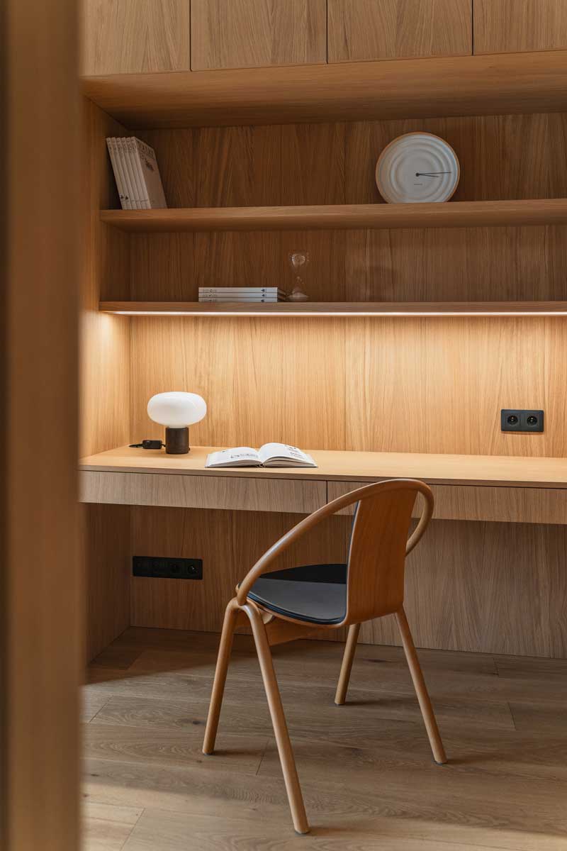 Detail vestavěného psacího stolu z dubového dřeva s policemi a integrovaným osvětlením.