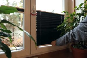 Detail ruky ovládající jednoduché černé stínění v okně garsonky.