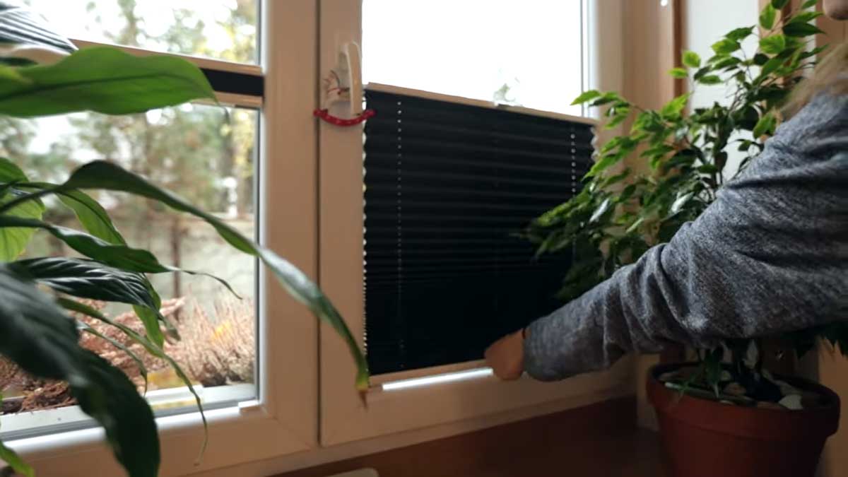 Detail ruky ovládající jednoduché černé stínění v okně garsonky.