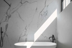 Samostatně stojící vana umístěná u velkého okna, obklopená mramorovým obkladem.