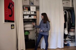 Otevřená šatna v garsonce plná boxů, polic a věšáků za závěsem.