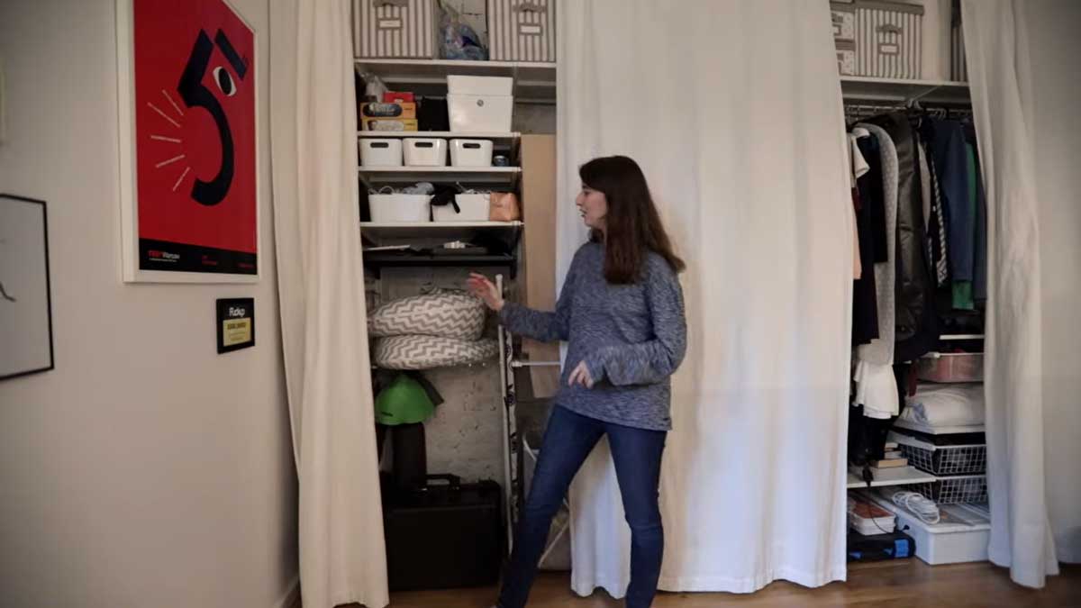 Otevřená šatna v garsonce plná boxů, polic a věšáků za závěsem.