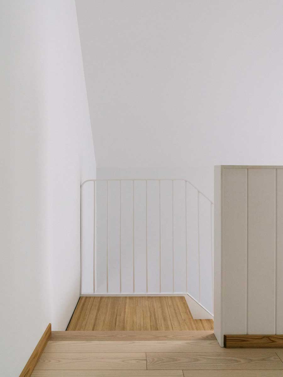 Minimalistické schodiště s bílým zábradlím a dřevěnou podlahou doplňuje čistotu interiéru.