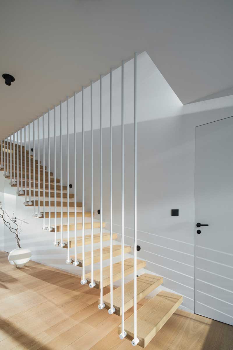 Zavěšené dřevěné schodiště s tenkými bílými pruty jako zábradlím.