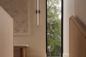 Schodiště s dřevěnými stupni, úzkým vertikálním oknem a minimalistickým nástěnným světlem