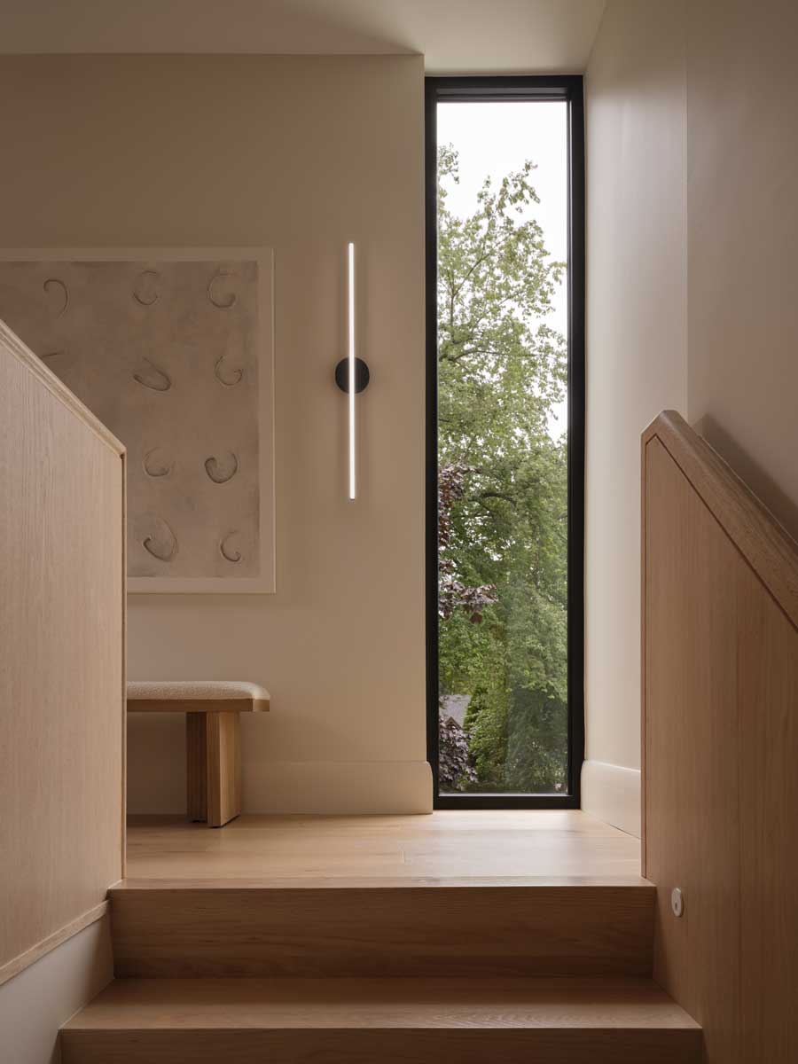 Schodiště s dřevěnými stupni, úzkým vertikálním oknem a minimalistickým nástěnným světlem
