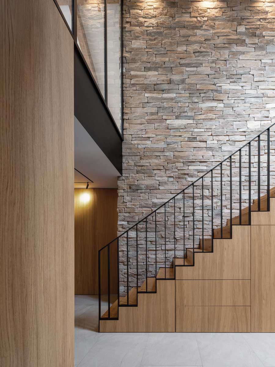 Detail schodiště se zabudovanými úložnými prostory a kamennou stěnou v interiéru.