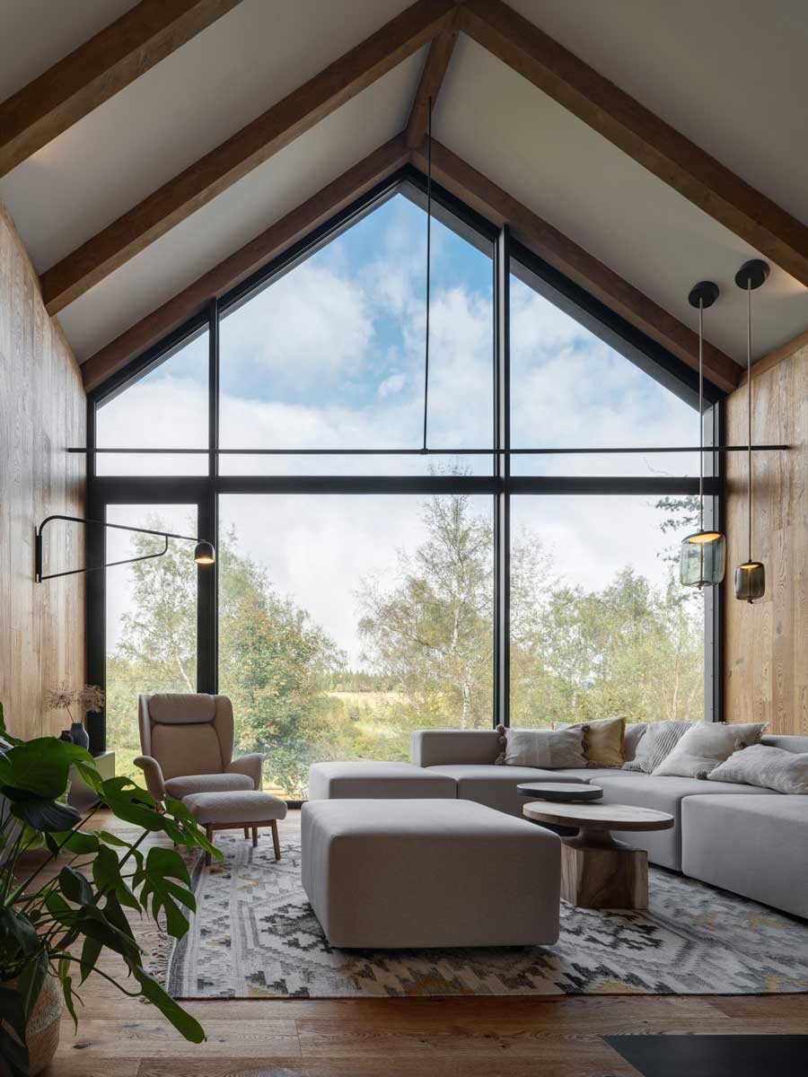 Sedačka orientovaná k velkému prosklenému štítu s výhledem na louky a lesy.