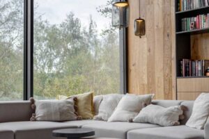 Moderní obývací pokoj s velkou rohovou sedačkou a celostěnným prosklením s výhledem do přírody.