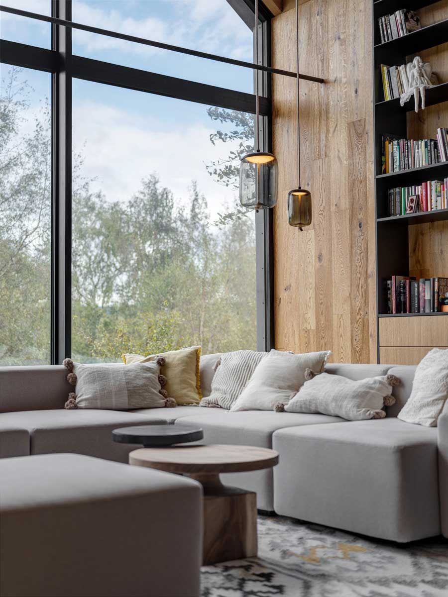 Moderní obývací pokoj s velkou rohovou sedačkou a celostěnným prosklením s výhledem do přírody.