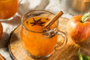 Sklenice horkého jablečného punče se skořicí, hvězdičkami badyánu a čerstvými jablky.