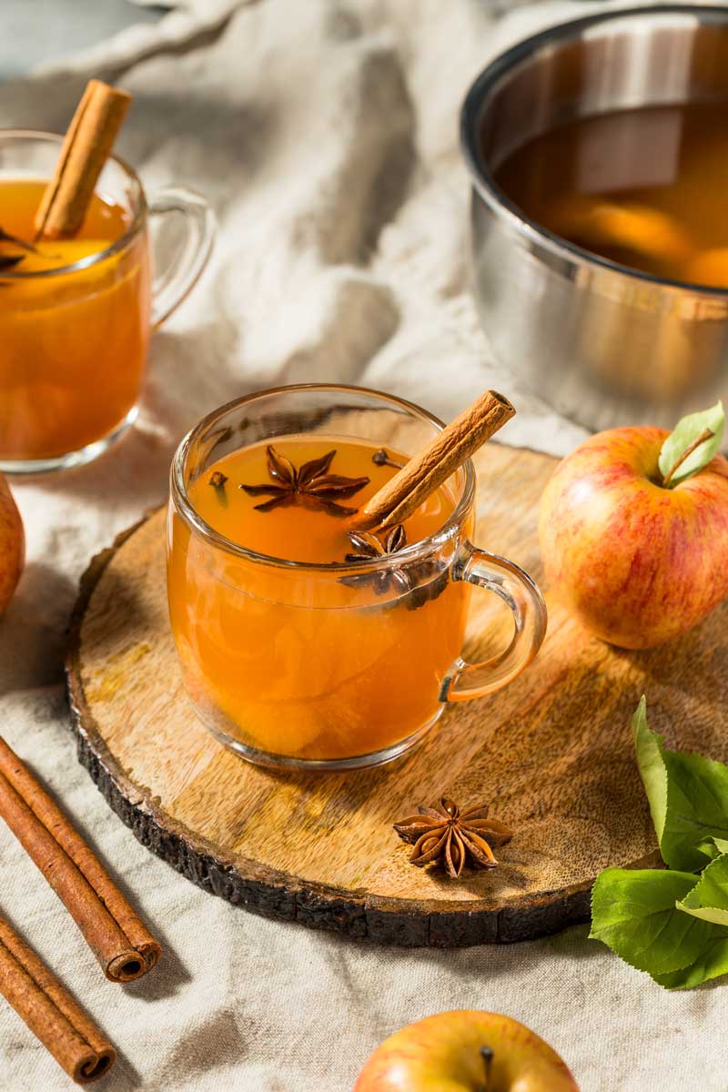Sklenice horkého jablečného punče se skořicí, hvězdičkami badyánu a čerstvými jablky.