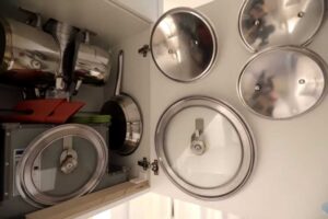 Vnitřek kuchyňské skříňky s promyšleným uložením hrnců, poklic a kuchyňských nástrojů.