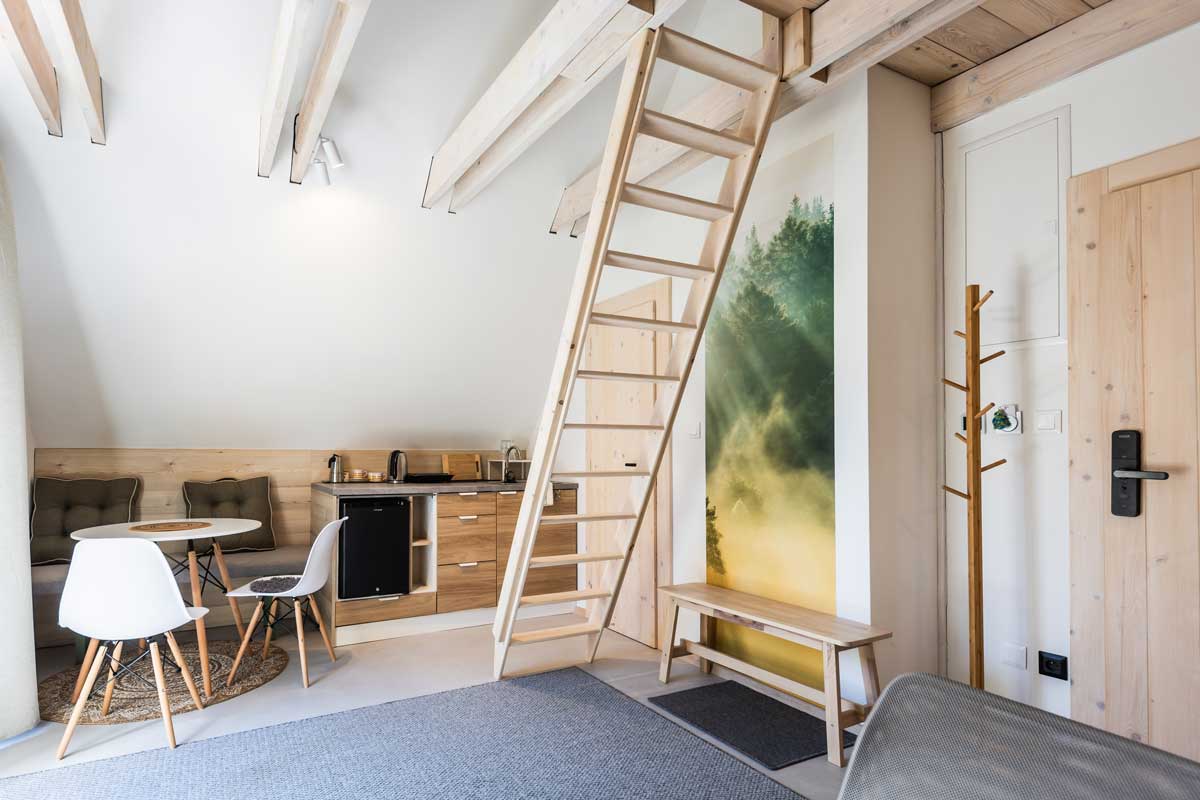 Společenský kout v horské chatě s lavicovým sezením, dřevěným stolem a betonovou stěnou