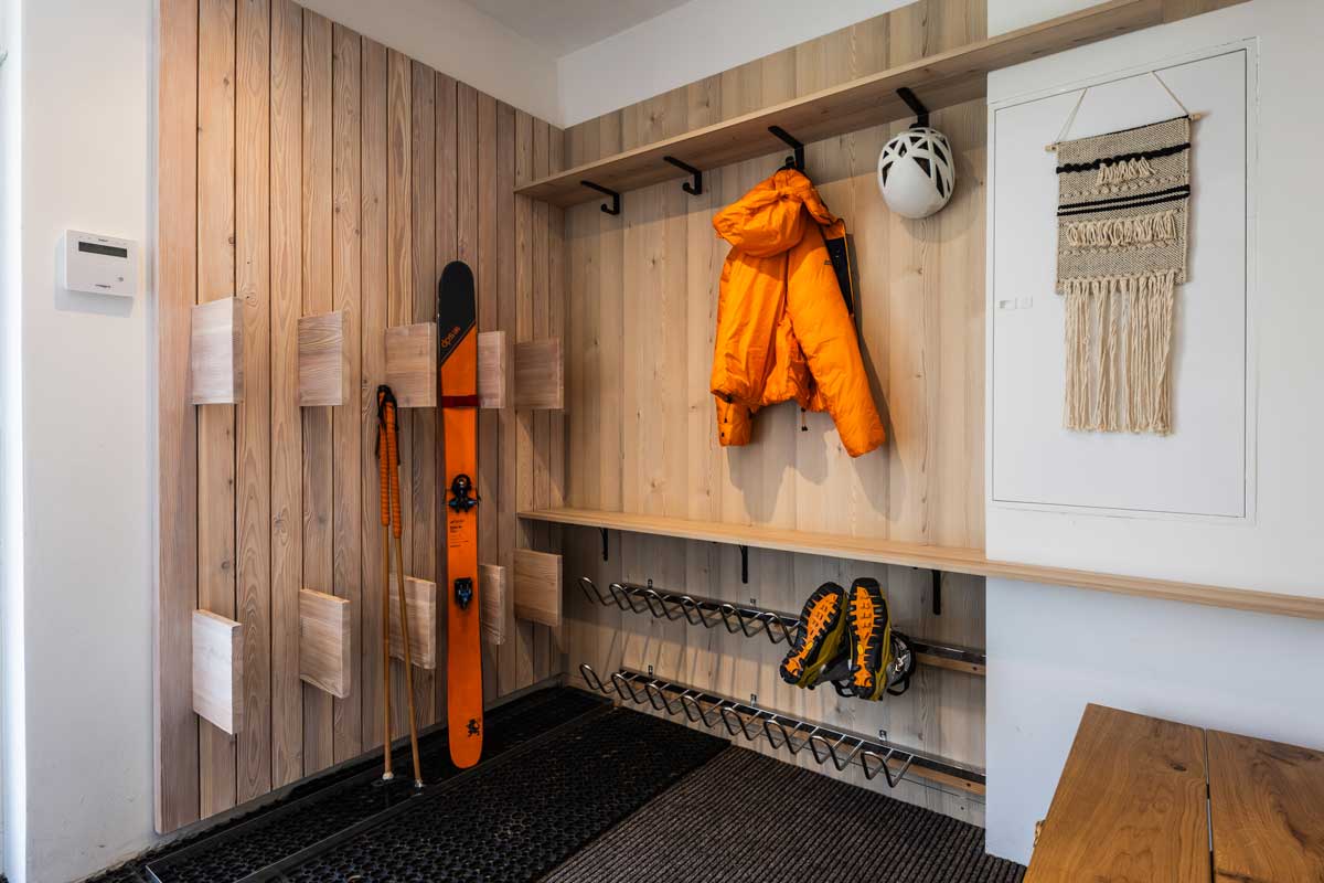Dřevěný stojan na lyže ve vstupní části chaty s lavicí, věšáky a místem na sušení bot