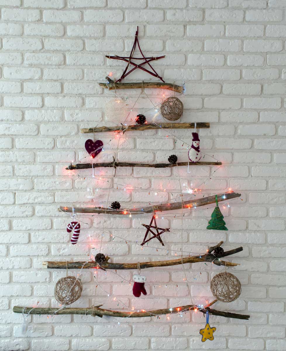 Vánoční stromeček vytvořený na zdi z přírodních větví jako úsporná dekorace do malého bytu.