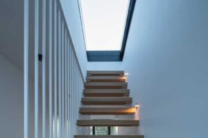 Dřevěné schodiště s bočním zábradlím vedeným k prosklenému světlíku.