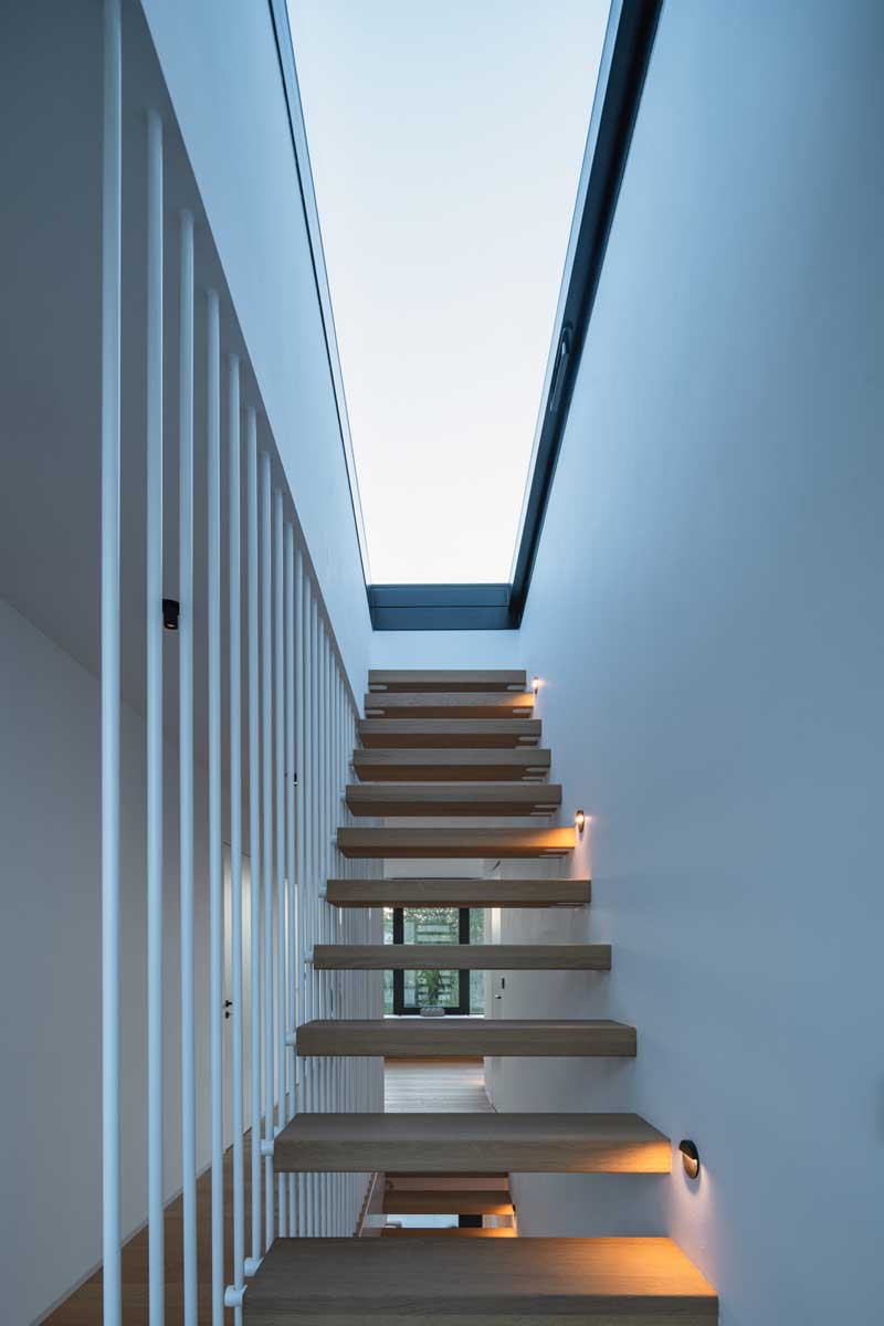 Dřevěné schodiště s bočním zábradlím vedeným k prosklenému světlíku.