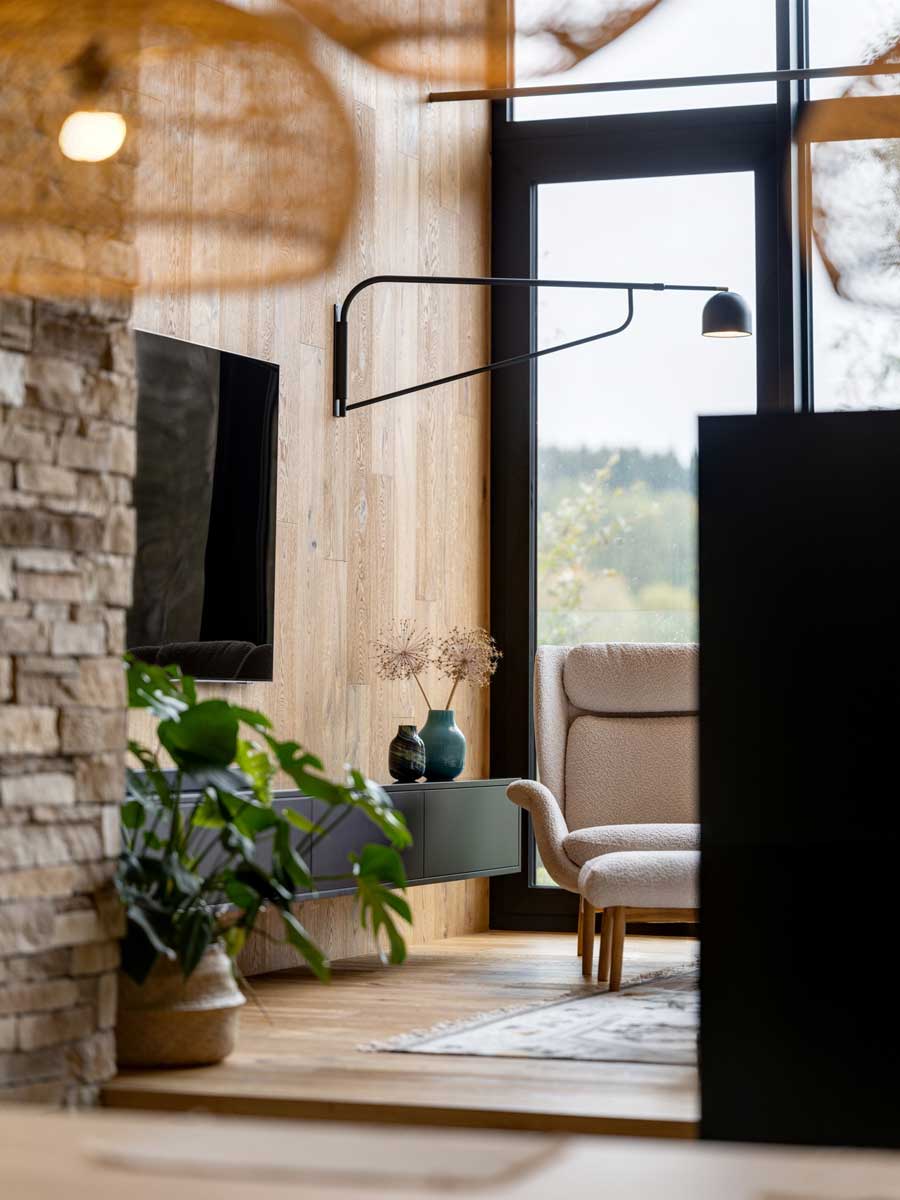 Designový koutek s moderní TV stěnou, křeslem a rostlinami u celoplošného okna.