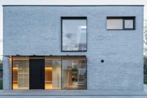 Pohled na fasádu domu s velkými okny a zastřešeným vstupem na terasu.