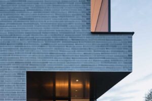 Posezení na kryté terase u prosklené stěny domu během soumraku.