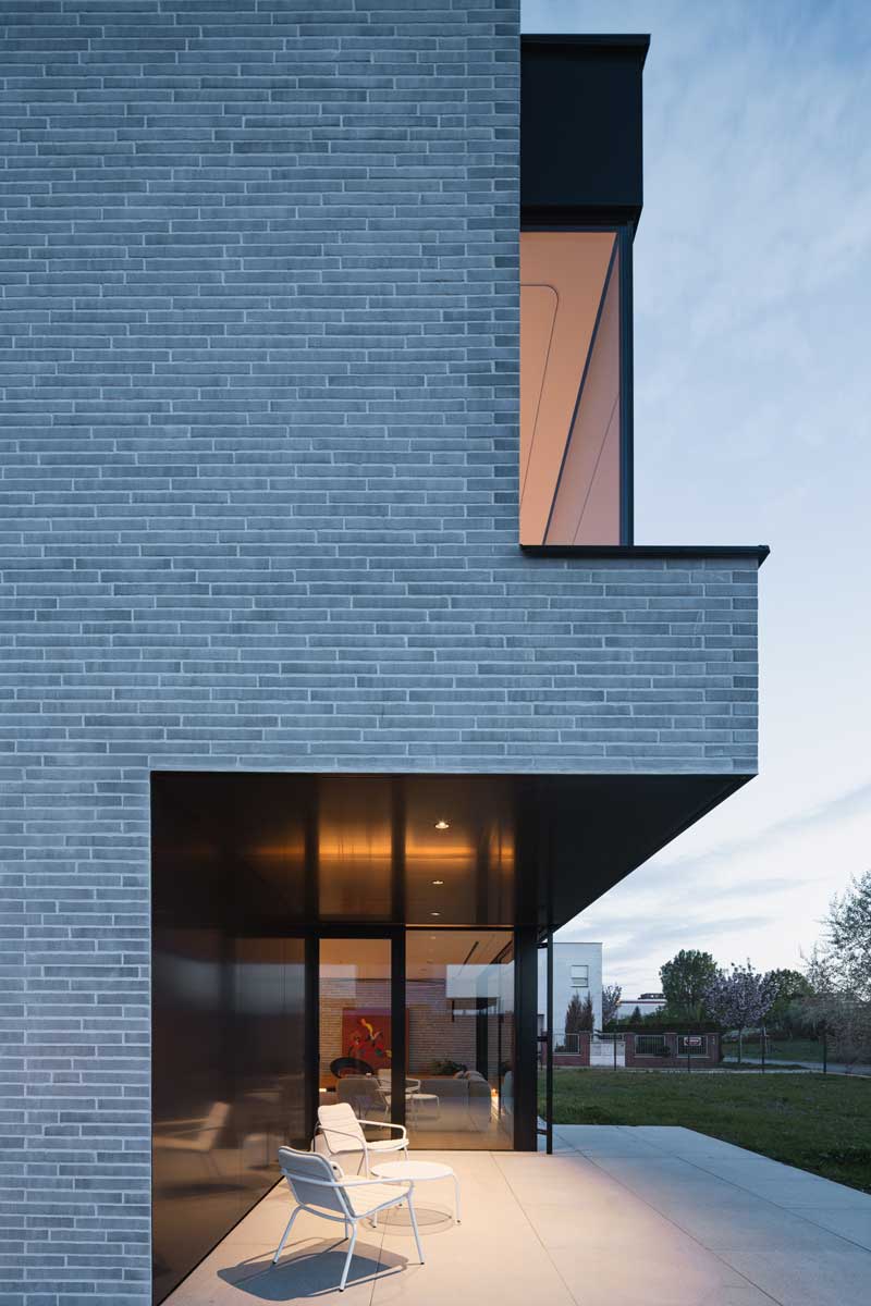 Posezení na kryté terase u prosklené stěny domu během soumraku.