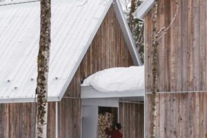 Majitel ukládá dřevo v krytém průchodu mezi dřevěnými objekty domu který přirozeně splývá se zasněženým prostředím