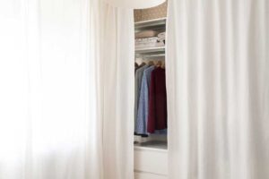 Vestavěné úložné prostory skryté za bílým závěsem v malé ložnici.