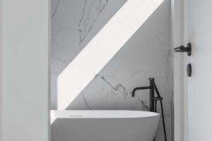 Detail samostatně stojící vany u mramorové stěny s dopadajícím ostrým světlem.