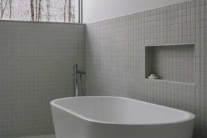 Volně stojící vana v minimalistické koupelně působí jako elegantní vyhlídka do zasněženého lesa a zvýrazňuje propojení interiéru s přírodou