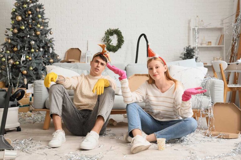 Unavený pár během vánočního úklidu sedící v nepořádku po oslavě.