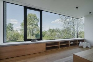 Velkoformátové okno s lavicí a úložnými prostory orientované do zeleně.