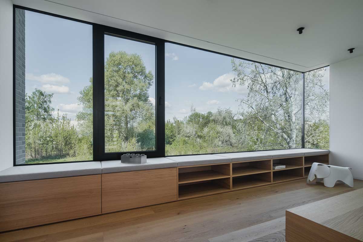 Velkoformátové okno s lavicí a úložnými prostory orientované do zeleně.