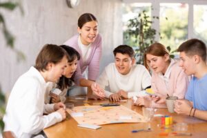 Skupina mladých lidí u velkého stolu hrajících deskové hry – ideální zimní prostor pro extroverty.