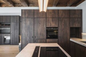 Vestavěné spotřebiče skryté v tmavých dřevěných skříních kuchyně