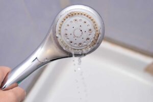 Sprchová hlavice zanesená zimním vodním kamenem způsobeným teplejší vodou a rychlejším srážením minerálů.