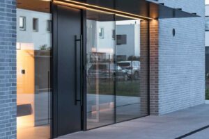 Hlavní vstupní portál domu s prosklenými plochami a černým přístřeškem.