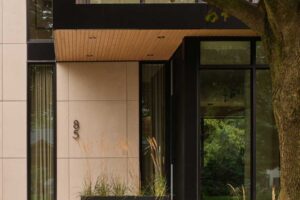 Detail vstupní části domu s kombinací světlého kamene, tmavého obkladu a dřevěného podhledu