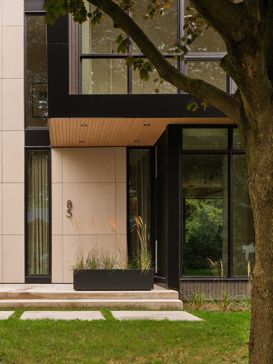 Detail vstupní části domu s kombinací světlého kamene, tmavého obkladu a dřevěného podhledu