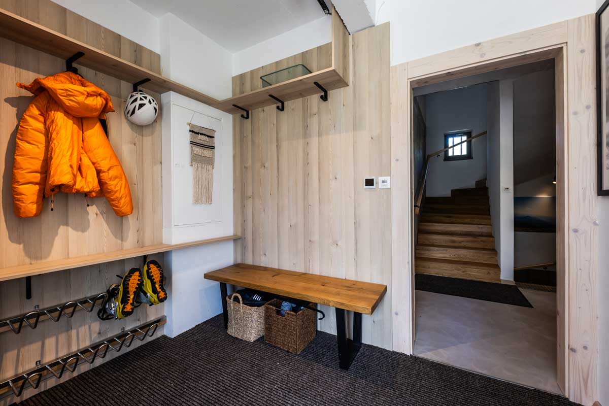Vstupní chodba horské chaty s dřevěnými obklady, lavicí, věšáky a úložným prostorem na obuv