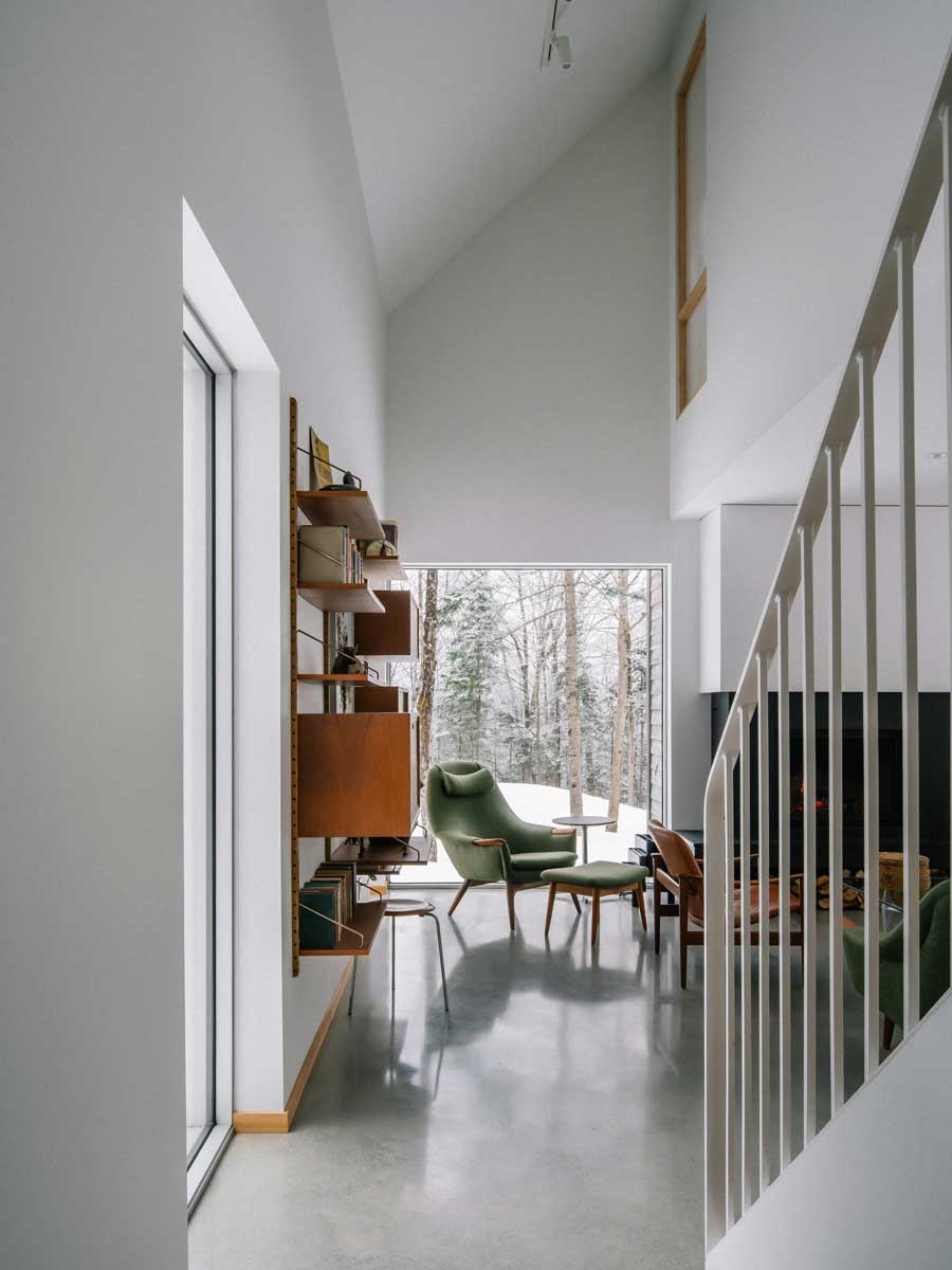 Světlý prostor u schodiště vede do čtecího koutu s ikonickým křeslem a velkým oknem které rámuje zimní les