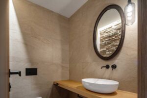 Moderní toaleta s keramickým umyvadlem, dřevěnou deskou a kamenným obkladem.