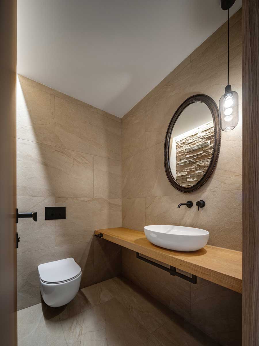 Moderní toaleta s keramickým umyvadlem, dřevěnou deskou a kamenným obkladem.